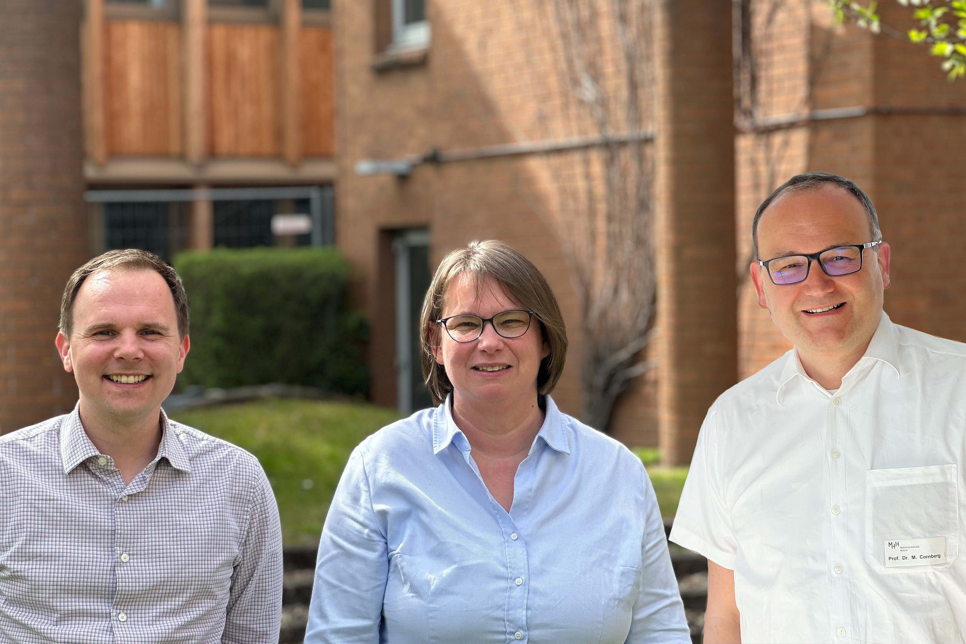 Group photo with three people standing side by side and a building in the background 