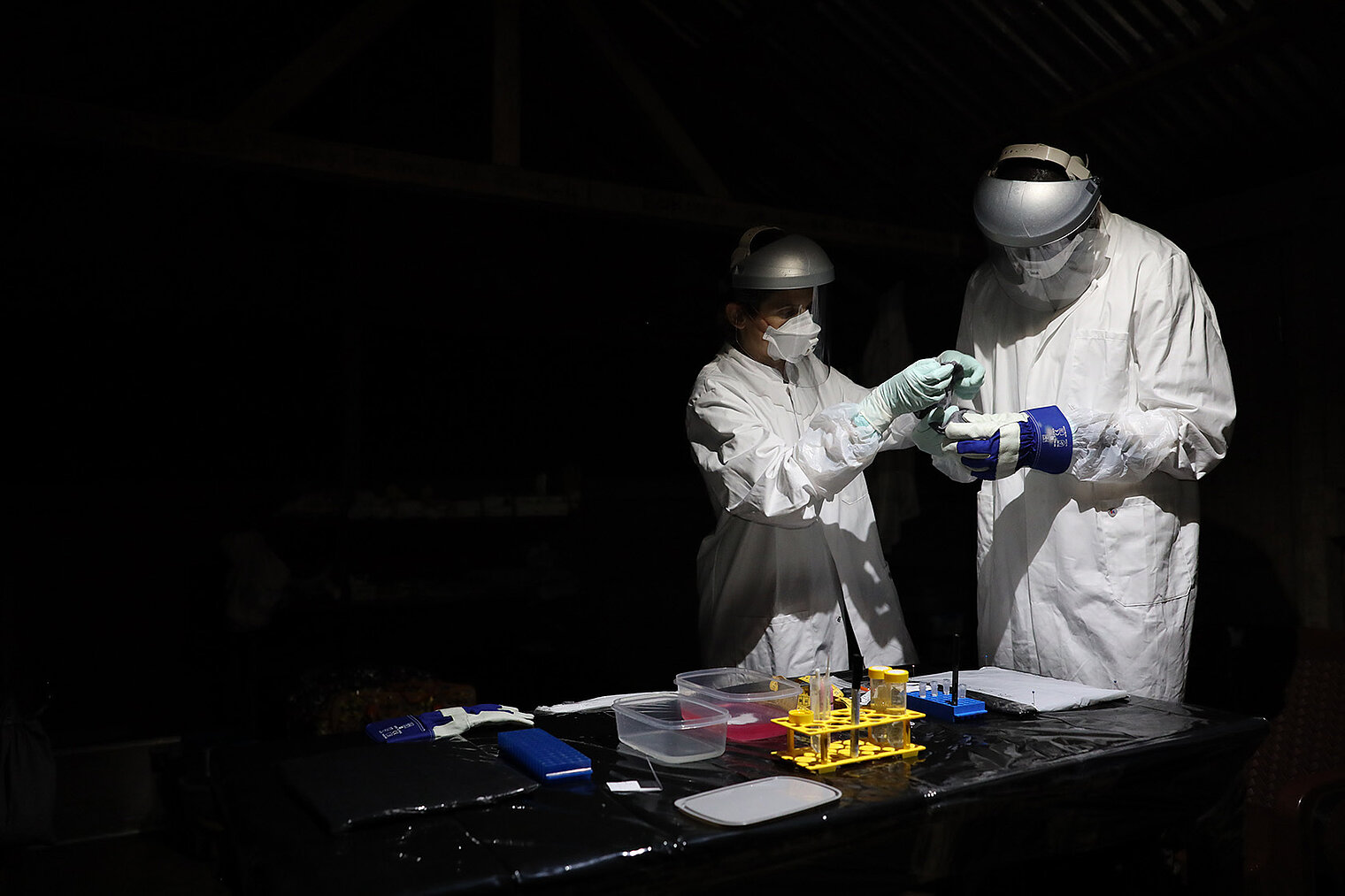 Two people wearing white protective clothing and carrying equipment for taking samples