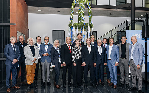 Gruppenbild mit 16 Personen, im Hintergrund die Richtkrone. 