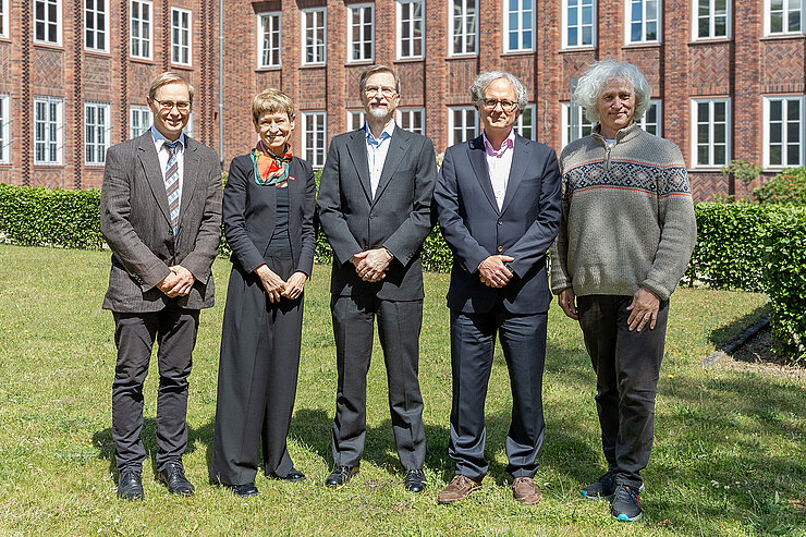 Gruppenfoto von vier Männern und einer Frau auf einer Wiese vor einem Backsteingebäude