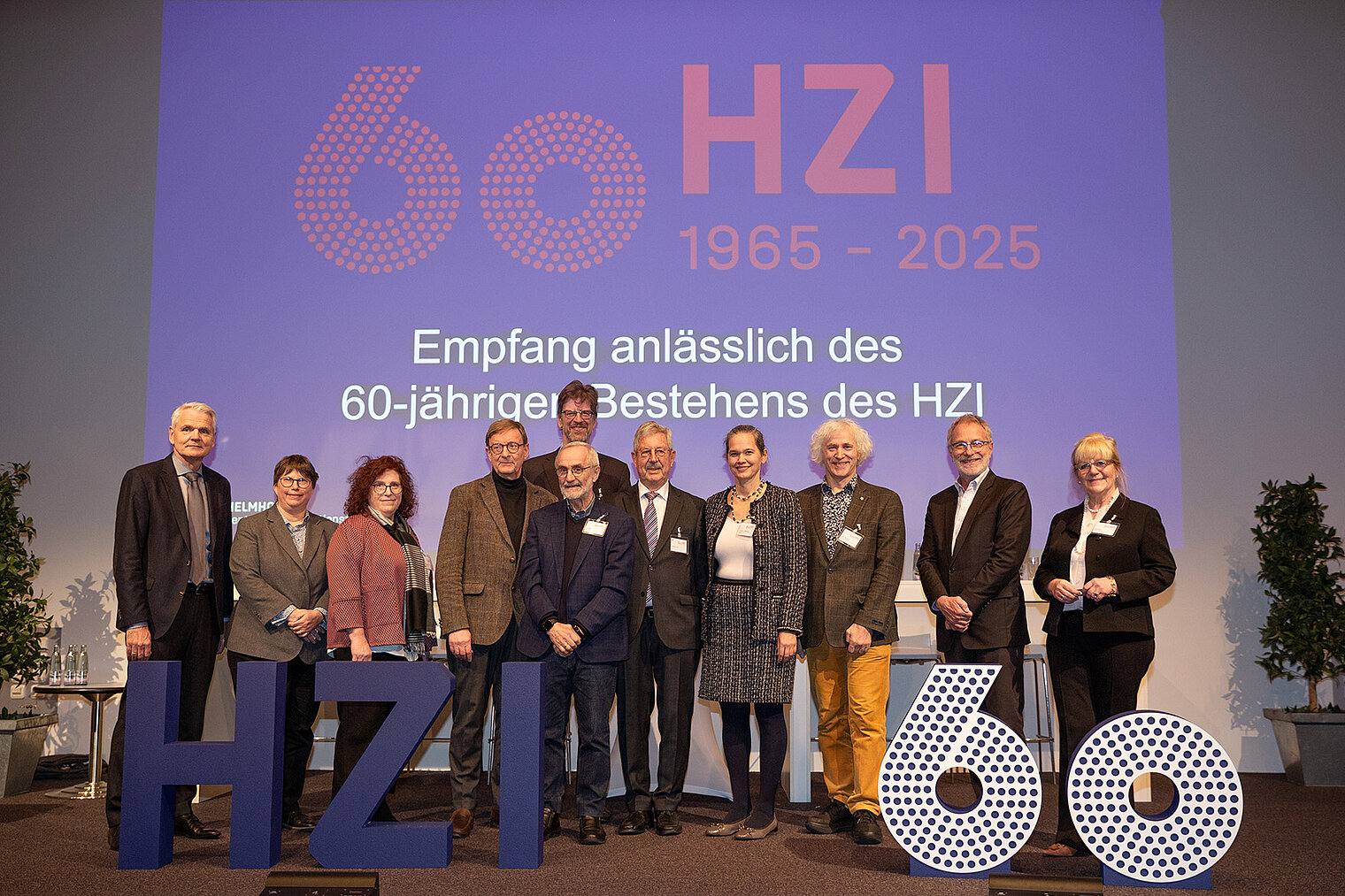 Gruppenbild mit 11 Personen hinter einem 3D-Schriftzug "HZI 60"