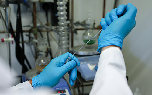  A view inside a laboratory; two hands wearing blue gloves working with a pipette