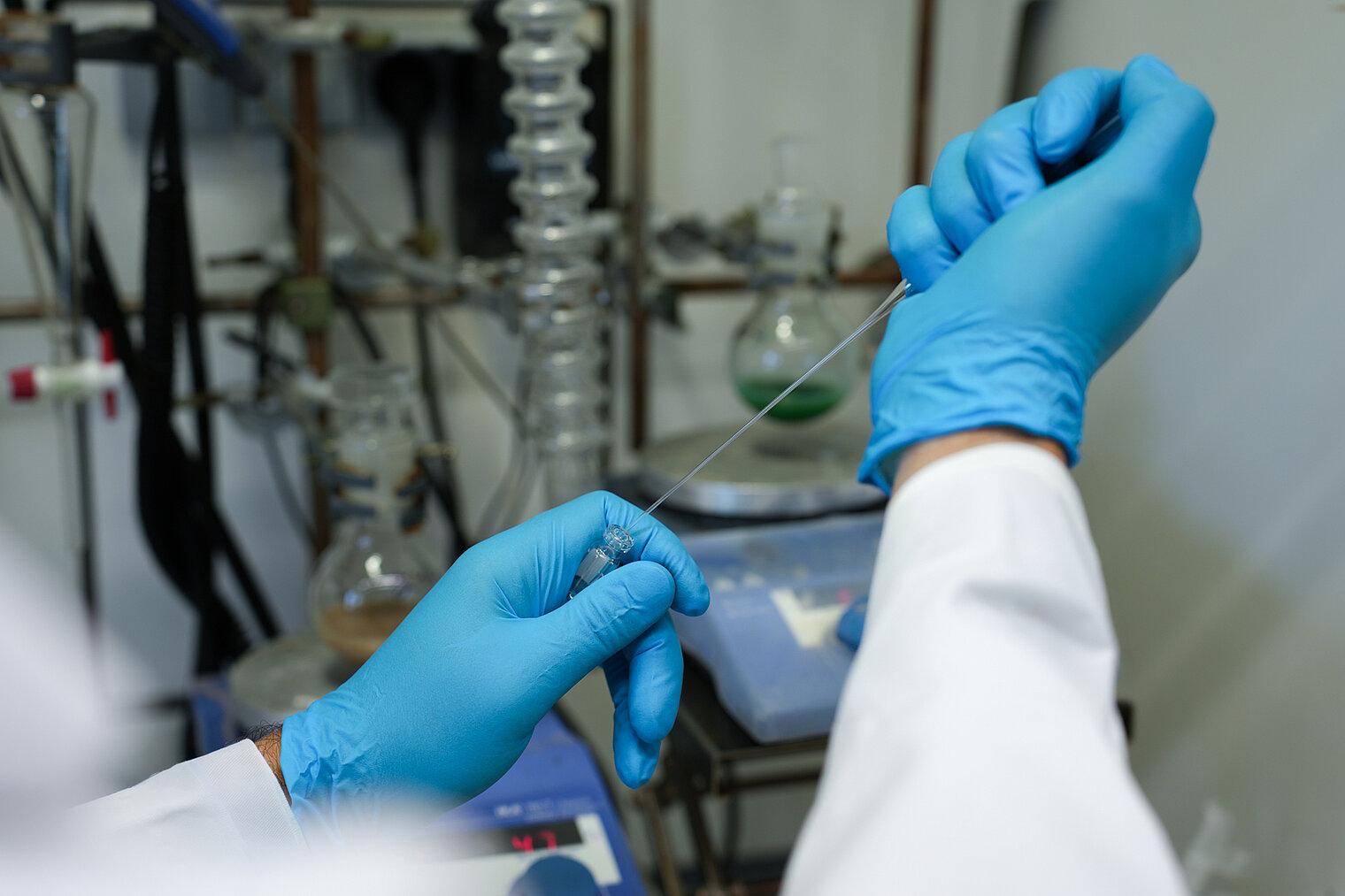 Einblick in ein Labor; zwei Hände mit blauen Handschuhen die mit einer Pipette arbeiten