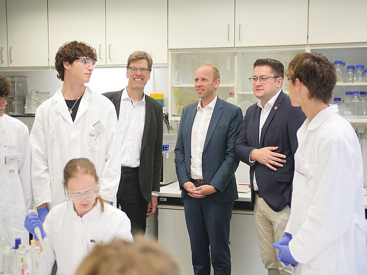 Three men in suits with students in lab coats