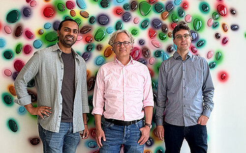Group photo with three men in front of a wall with colorful dots