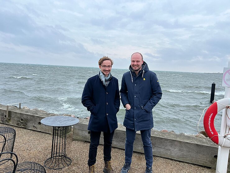 Zwei Personen auf einem Steinweg vorm Meer 