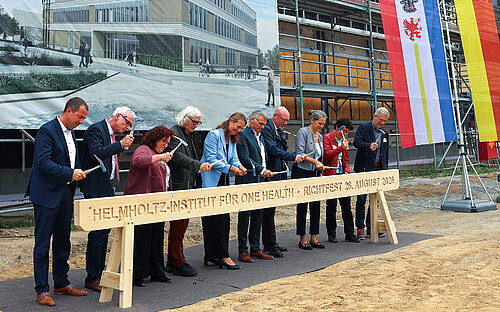 Nine people at a topping-out ceremony on a construction site symbolically strike a wooden beam with hammers.