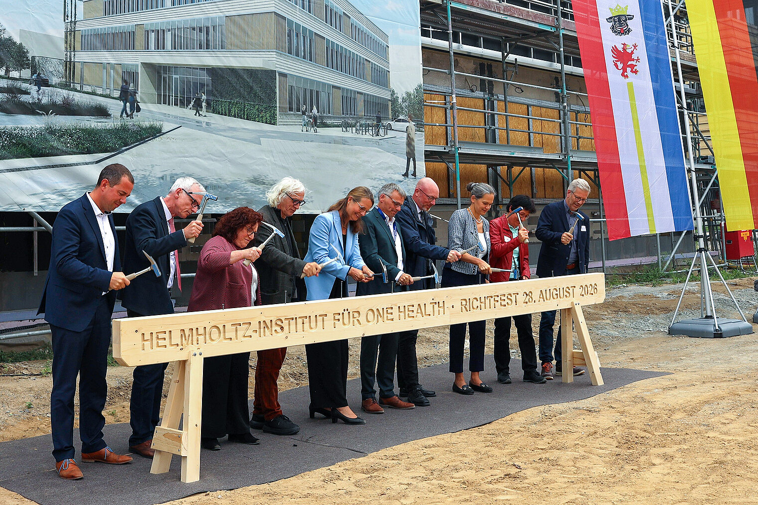 Nine people at a topping-out ceremony on a construction site symbolically strike a wooden beam with hammers.