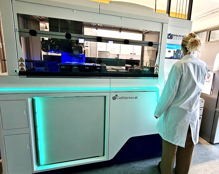 A woman wearing a lab coat is standing in front of a cell culture robot in the lab