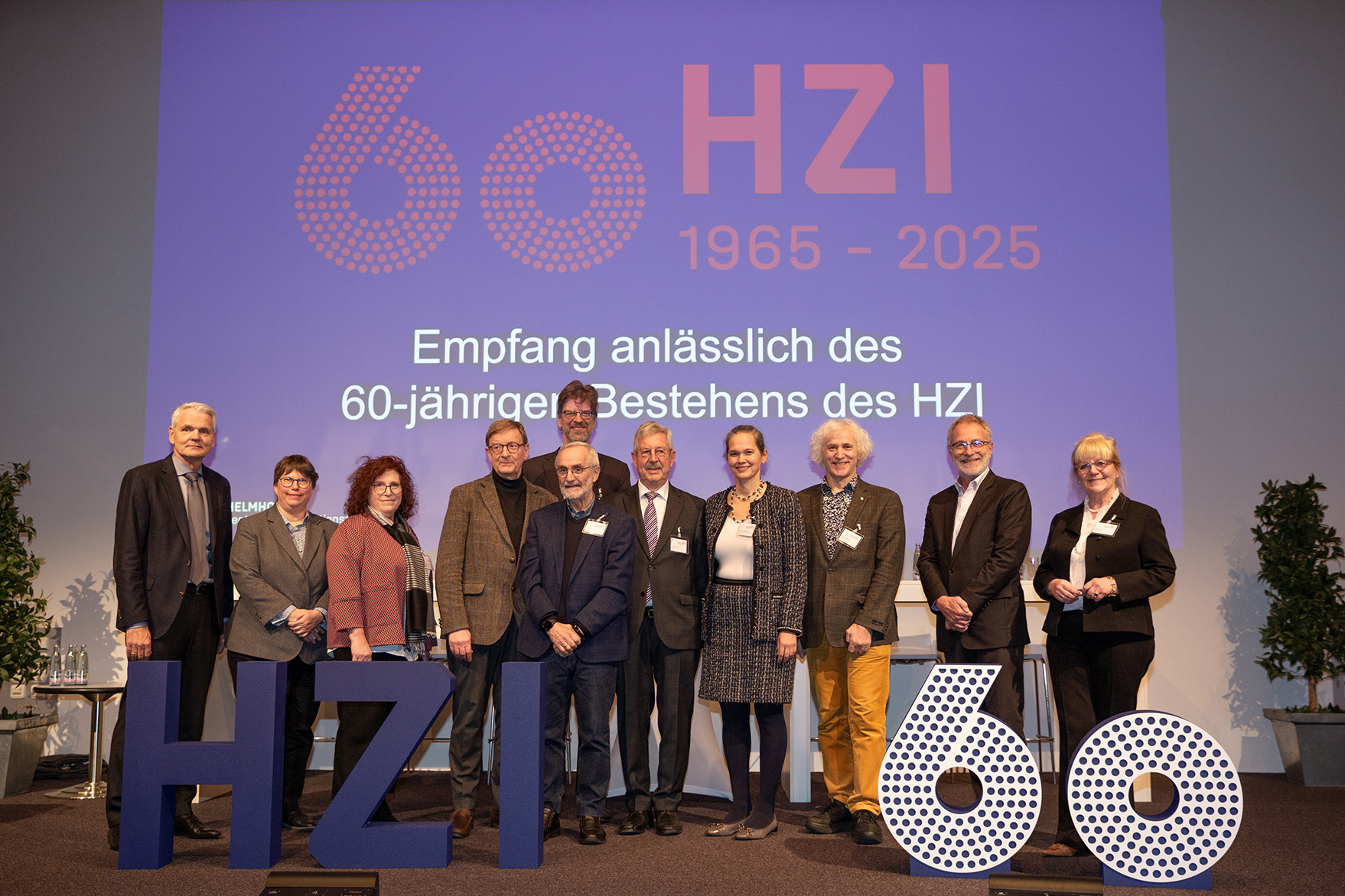 Gruppenbild mit 11 Personen hinter einem 3D-Schriftzug "HZI 60"